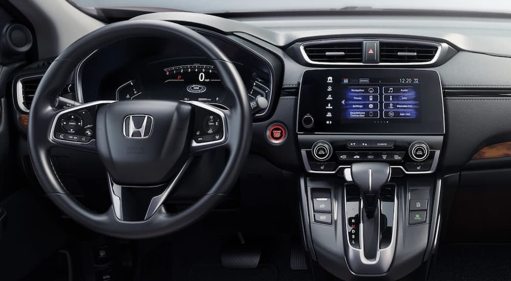 The black interior of a 2022 Honda CR-V Touring shows the steering wheel and infotainment screen.