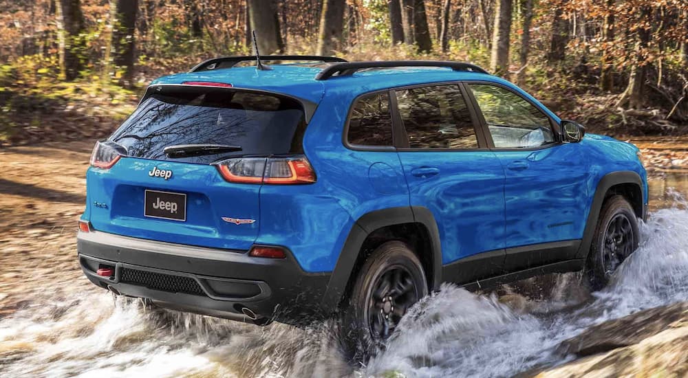 A blue 2022 Jeep Cherokee Trailhawk is shown from the rear driving through a river.