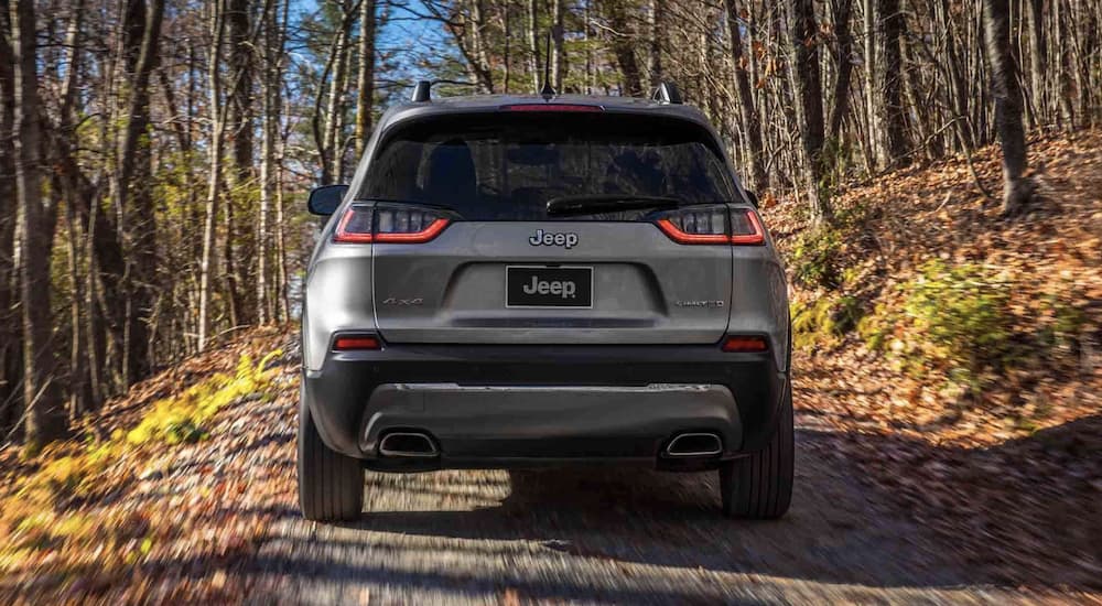 A grey 2022 Jeep Cherokee Limited is shown from the rear driving on a dirt road.
