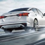 A white 2022 Nissan Altima is shown from the rear driving on a snowy road.