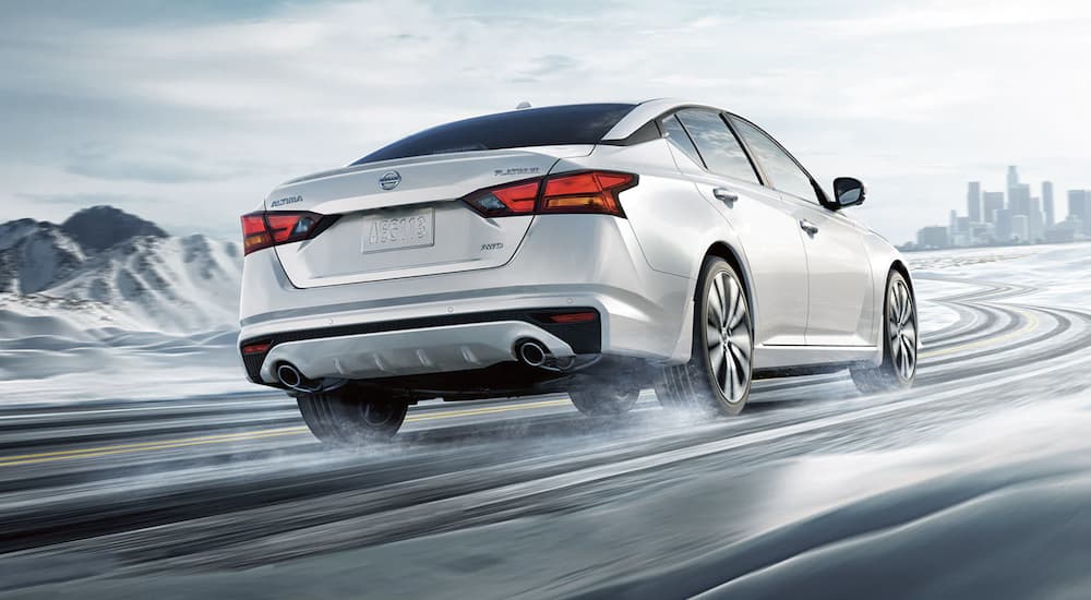 A white 2022 Nissan Altima is shown from the rear driving on a snowy road.