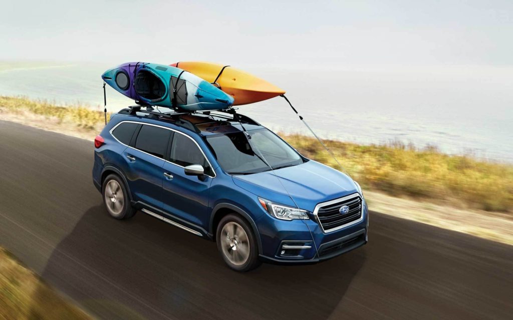 A blue 2022 Subaru Ascent Touring is shown driving with two kayaks on the roof.