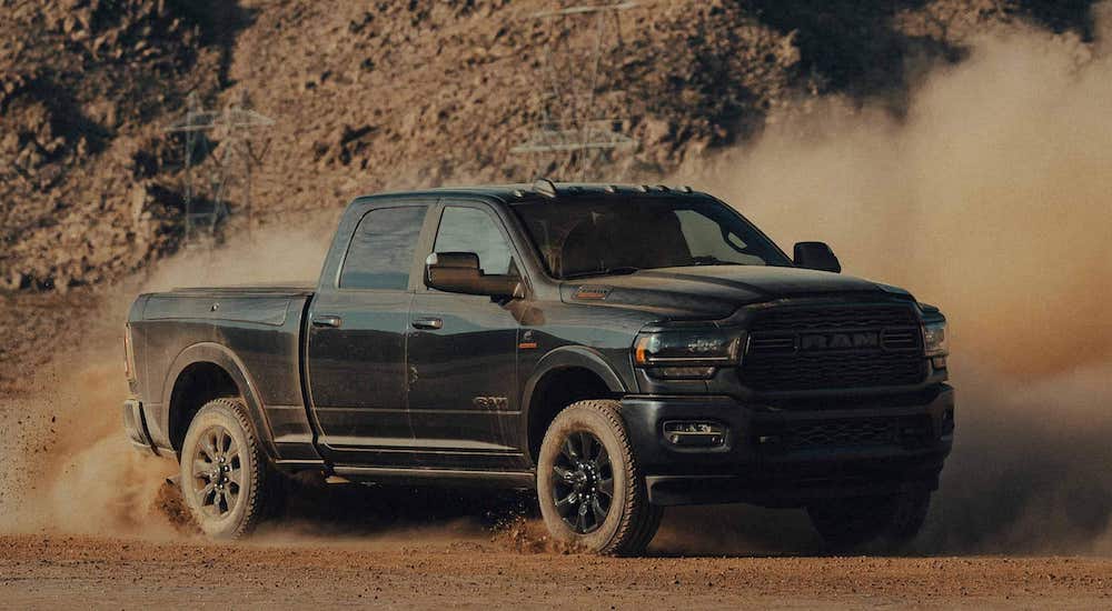 A black 2022 Ram 2500 is shown from the front at an angle while kicking up dust off-road after leaving a Ram dealer.