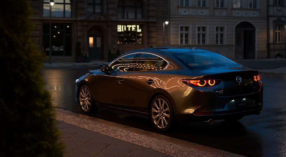 A grey 2022 Mazda3 sedan is shown from the rear at night on a city street.
