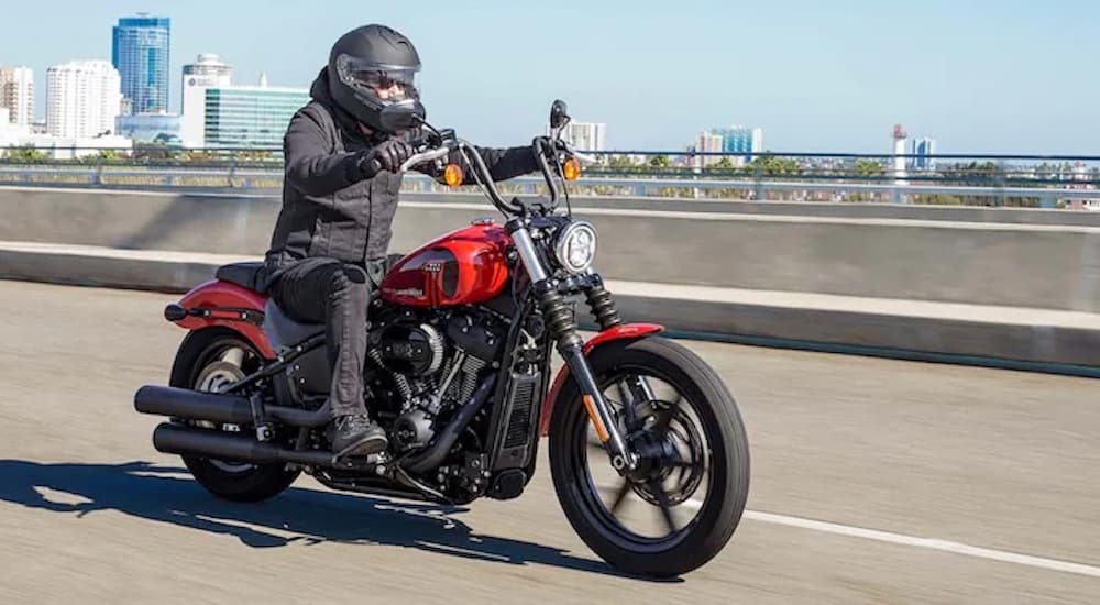 A red 2022 Harley Davidson Street Bob is shown from the front at an angle while driving down the highway after leaving a Harley-Davidson dealership.
