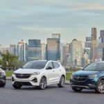 A blue, white, and grey 2023 Buick Encore GX are shown parked overlooking a city.