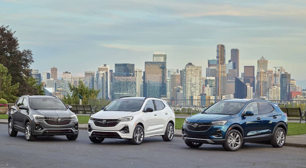 A blue, white, and grey 2023 Buick Encore GX are shown parked overlooking a city.