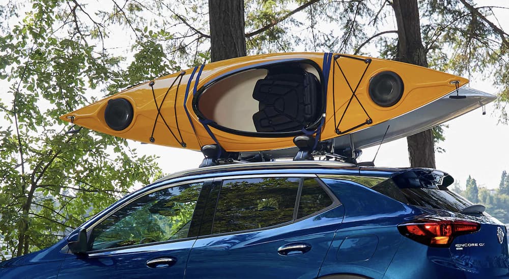 A blue 2023 Buick Encore GX is shown driving with a yellow kayak on the roof.