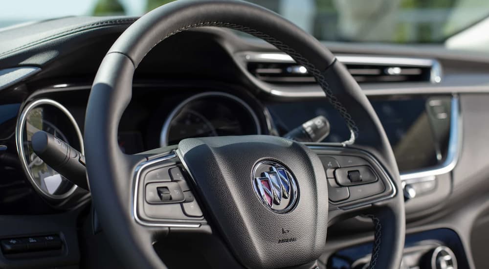 The black interior of a 2023 Buick Encore GX shows the steering wheel and infotainment screen.