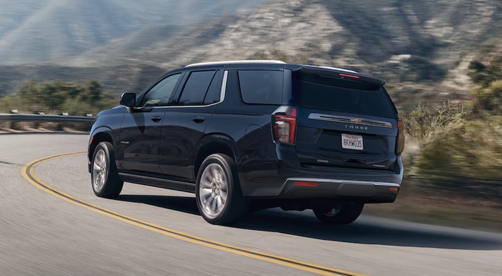 A black 2023 Chevy Tahoe is shown from the rear driving on an open road.