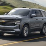 A silver 2023 Chevy Tahoe is shown from the front driving on an open road.