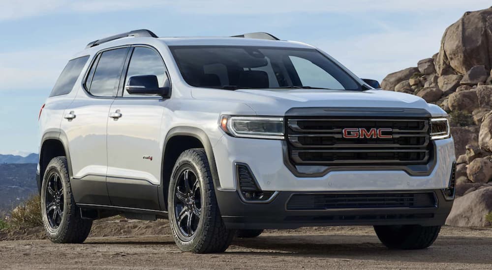 A white 2023 GMC Acadia AT4 is shown from the front parked under a blue sky.