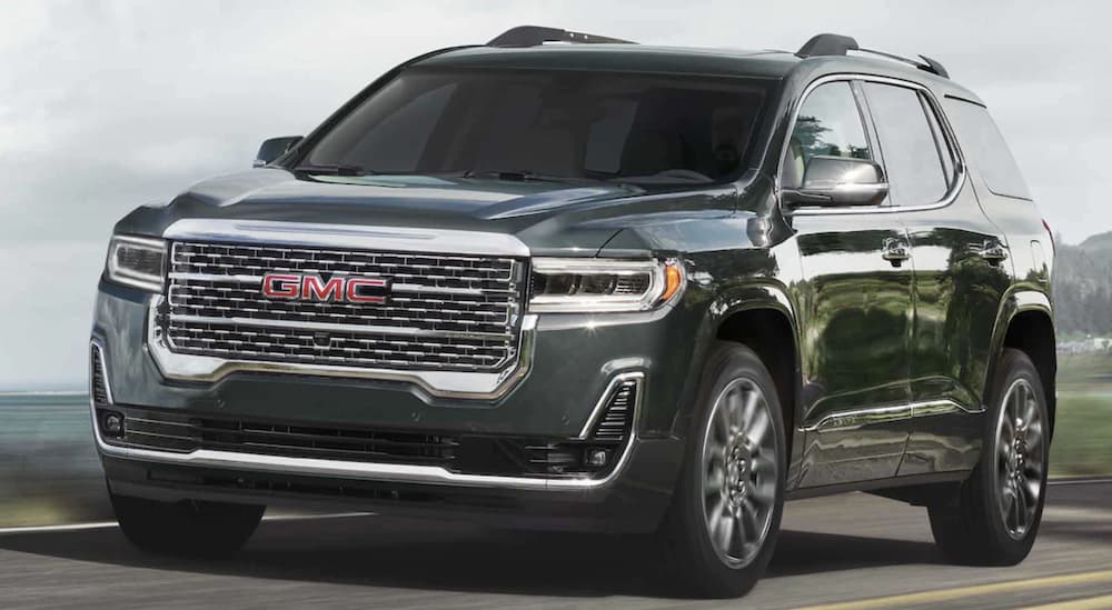 A black 2023 GMC Acadia is shown driving on an open road.