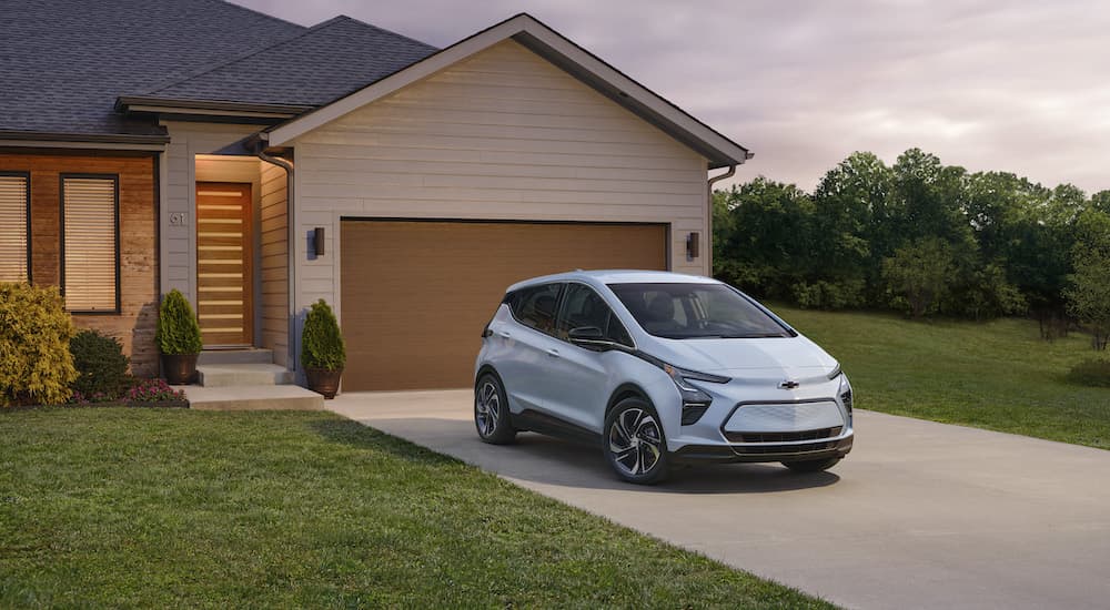 A blue 2023 Chevy Bolt EV is shown from the front at an angle while parked in front of a house.