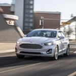 A white 2020 Ford Fusion is shown from the front while rounding a corner after the owner searched for 'used car dealership near me'.