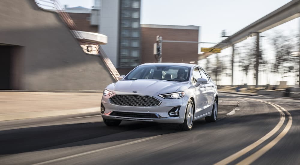 A white 2020 Ford Fusion is shown from the front while rounding a corner after the owner searched for 'used car dealership near me'.