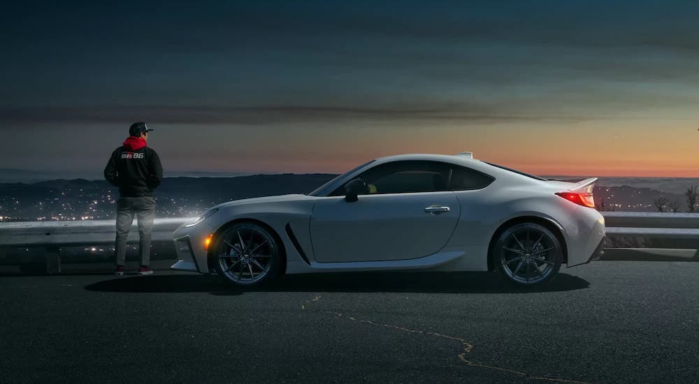 A white 2022 Toyota GR86 is shown from the side while parked on a city overlook.