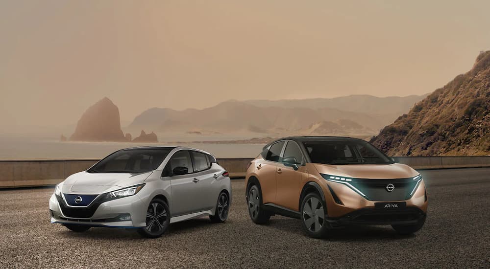 A white 2022 Nissan LEAF and bronze Ariya are shown parked near the ocean.
