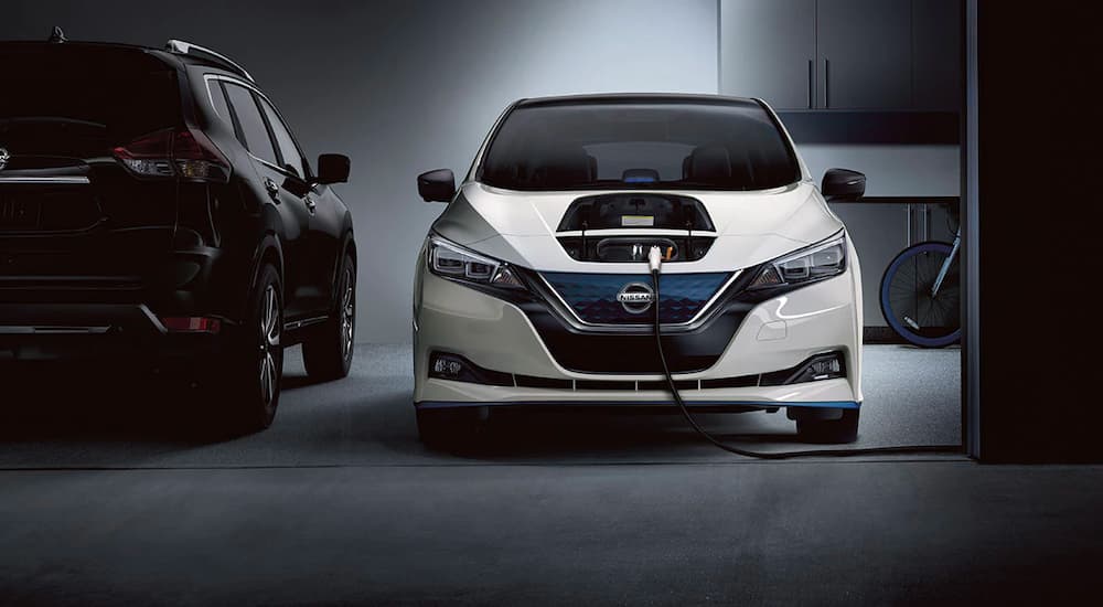 A WHITE 2022 Nissan LEAF is shown charging in a garage after visiting a Nissan dealer.