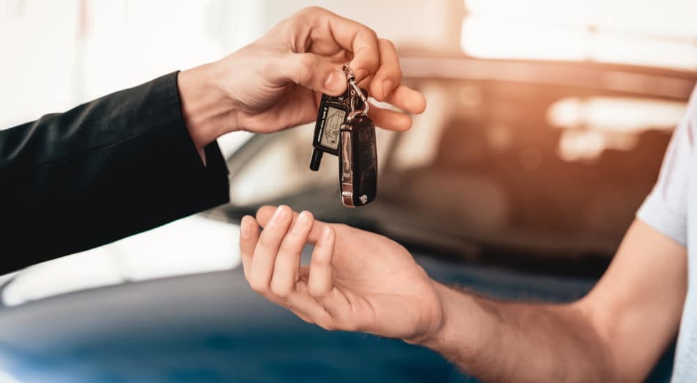 A salesman is shown handing a car key to a customer.