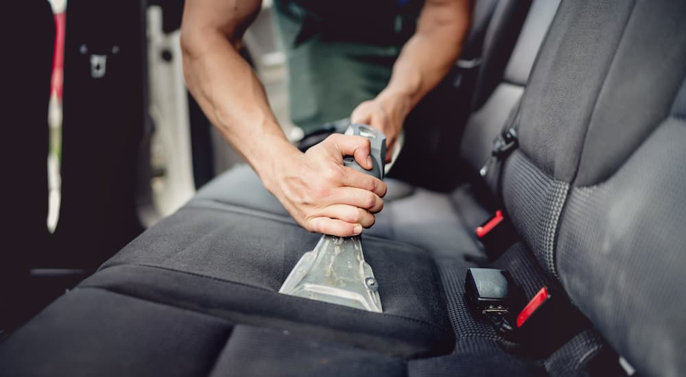 A person is shown vacuuming the back seat of a car.