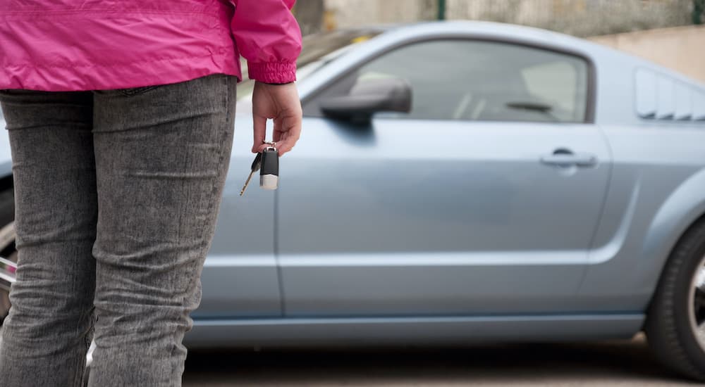 A person is shown holding a car key in front of a blue car after deciding to search 'sell my car.'