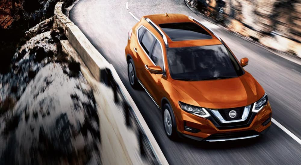 An orange 2020 Nissan Rogue is shown from the front driving on an open road after searching 'sell my car.'