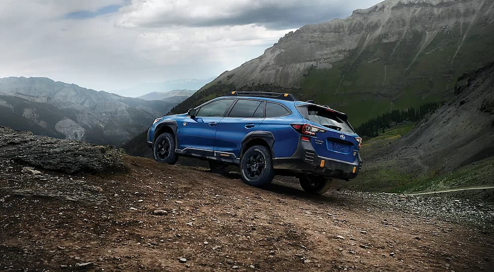 A blue 2022 Subaru Outback Wilderness is shown from the rear driving on a dirt trail.