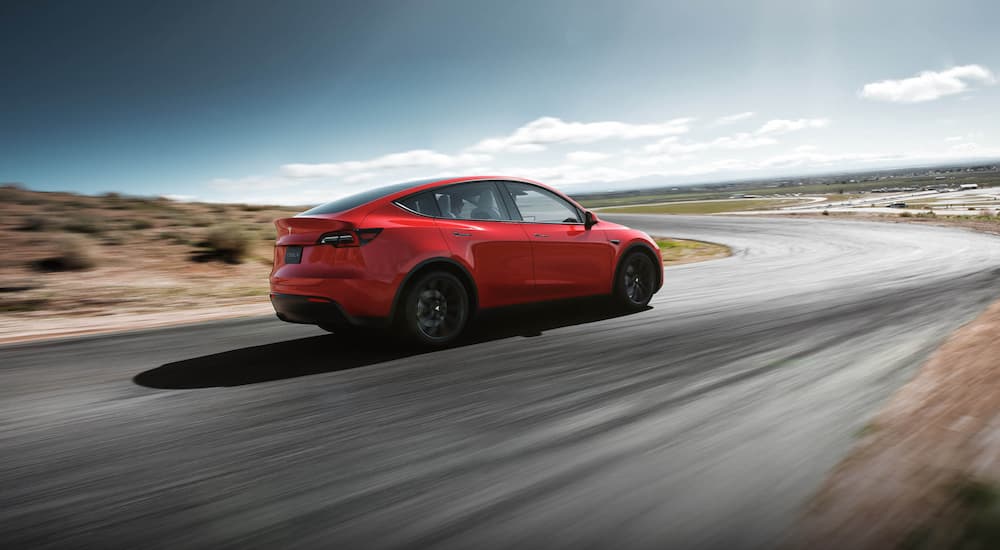 A red Tesla Model Y is shown from the rear driving on an open highway.