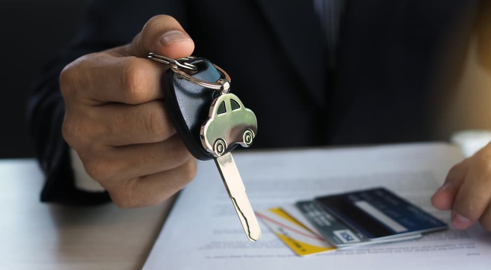 A salesman is shown holding a car key while looking over paperwork.