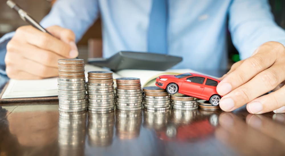 A red toy car is shown on a stack of coins.