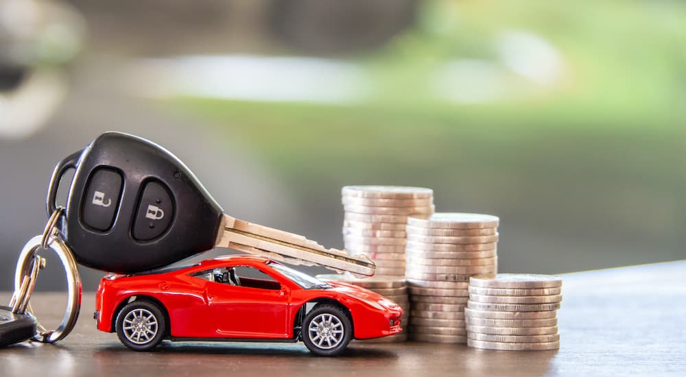 A toy car is shown next to a stack of coins and a car key.