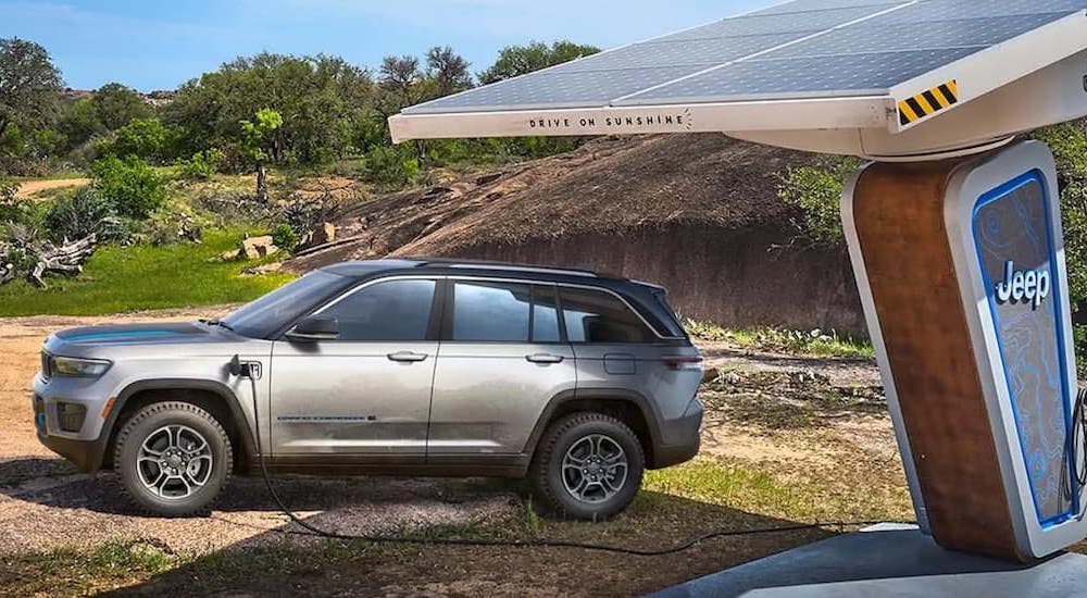 A silver 2022 Jeep Grand Cherokee 4xe is shown from the side while charging after leaving a dealer that advertised off-road vehicles for sale.