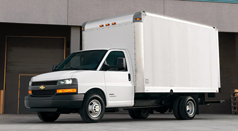 A white 2022 Chevy Express Cutaway Van is shown at a dealer with commercial trucks for sale.