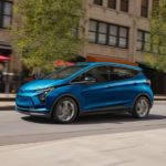 A blue 2023 Chevy Bolt EV is shown driving on a city street.