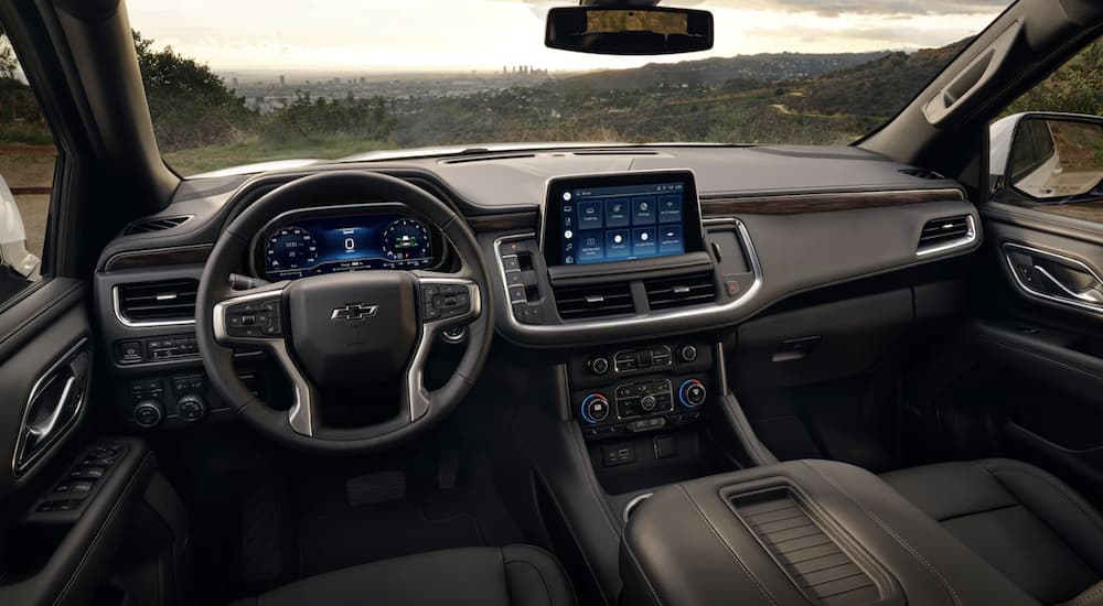 The black interior of a 2023 Chevy Tahoe shows the steering wheel and infotainment screen.