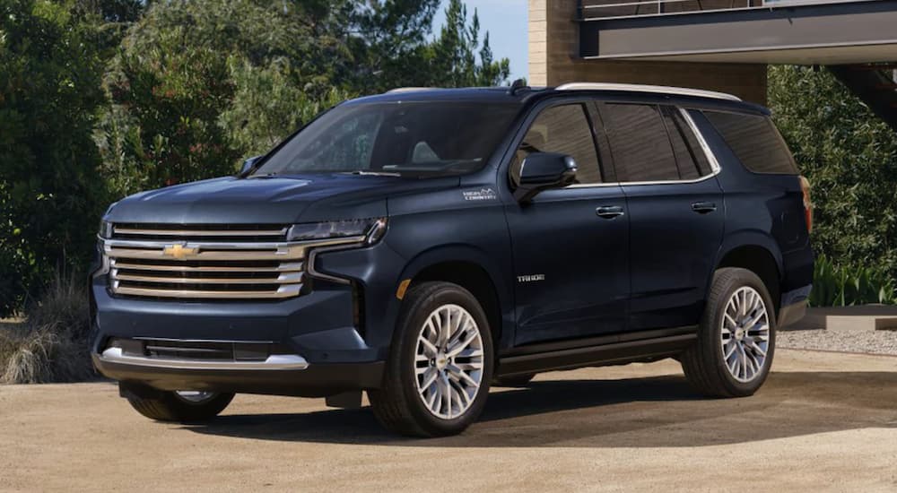 A blue 2023 Chevy Tahoe High Country is shown parked in front of a building.