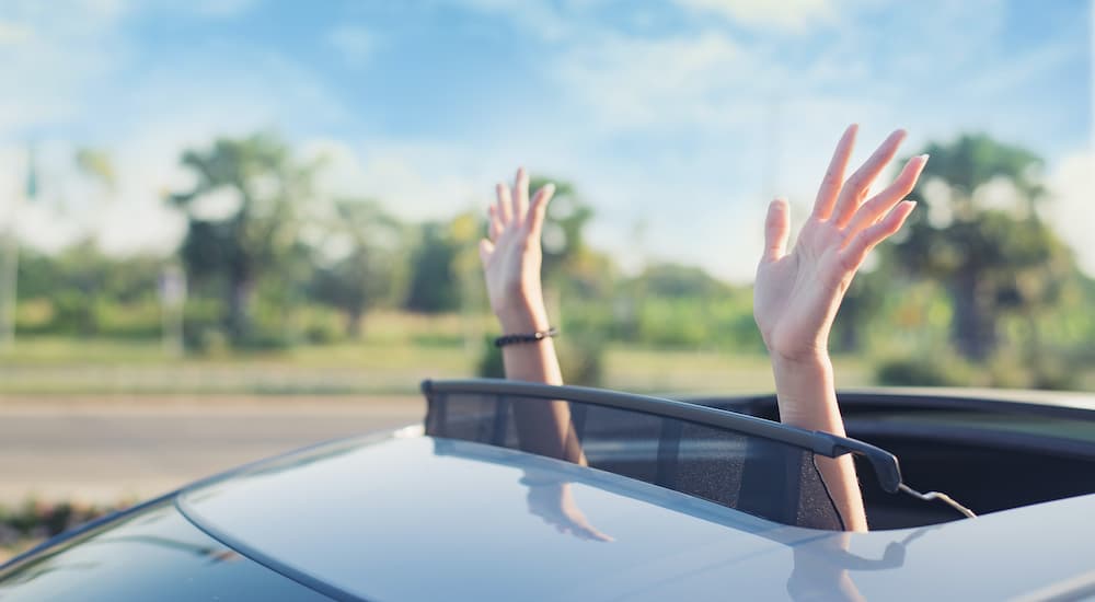 A person is shown putting their hands out of a sunroof.
