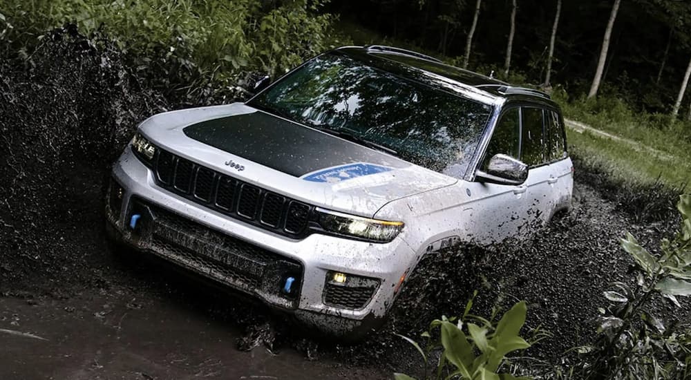 A white 2023 Jeep Grand Cherokee Two-Row is shown off-roading through a muddy river.