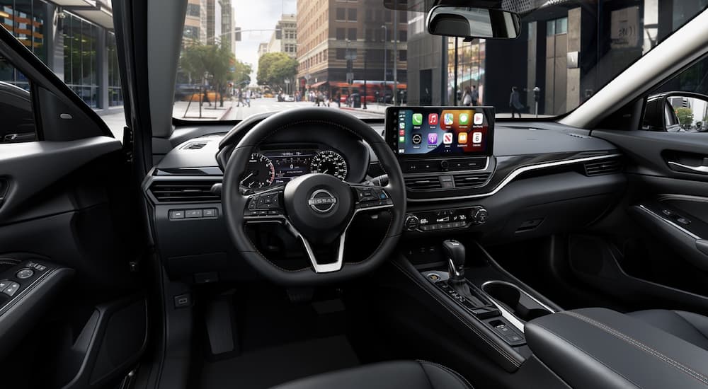 The black interior of a 2023 Nissan Altima shows the steering wheel and infotainment screen.