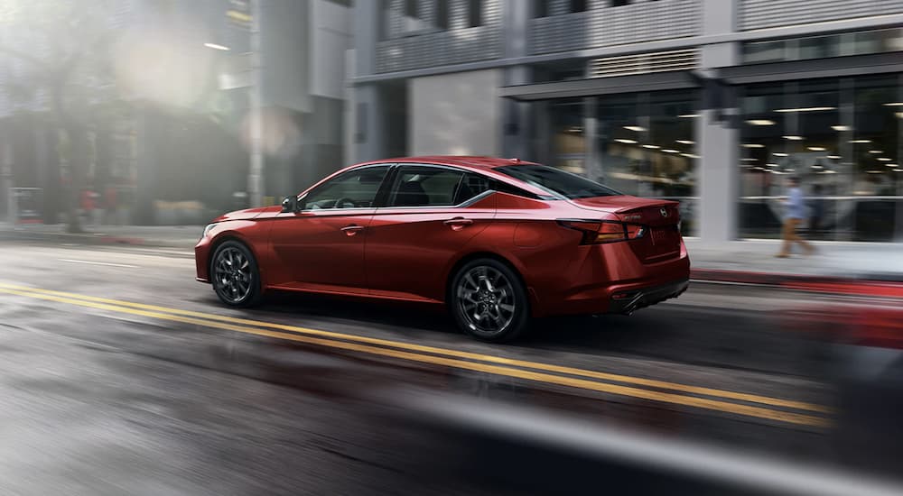 A red 2023 Nissan Altima is shown from the side driving through a city.