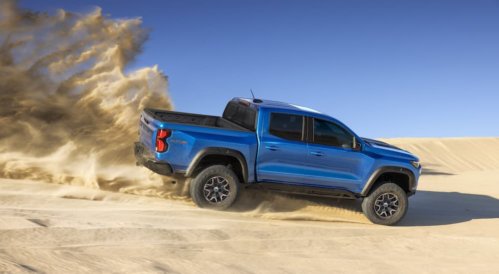 A blue 2023 Chevy Colorado ZR2 is shown from the side as it kicks up sand.