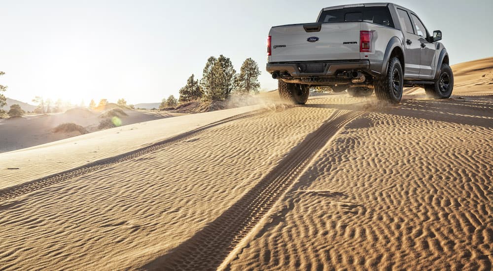 A white 2017 Ford F-150 Raptor is shown making tracks through sand.