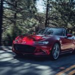 A red 2022 Mazda MX-5 Miata is shown driving on a tree-lined road.