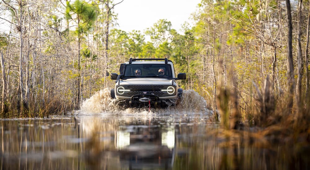A pale green 2022 Ford Bronco Everglades is shown driving through a marsh after leaving a Ford dealer.