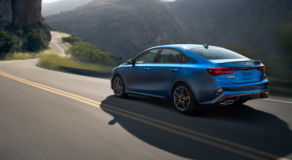 A popular Kia Forte for sale, a blue 2023 Kia Forte GT, is shown driving on a mountain road.