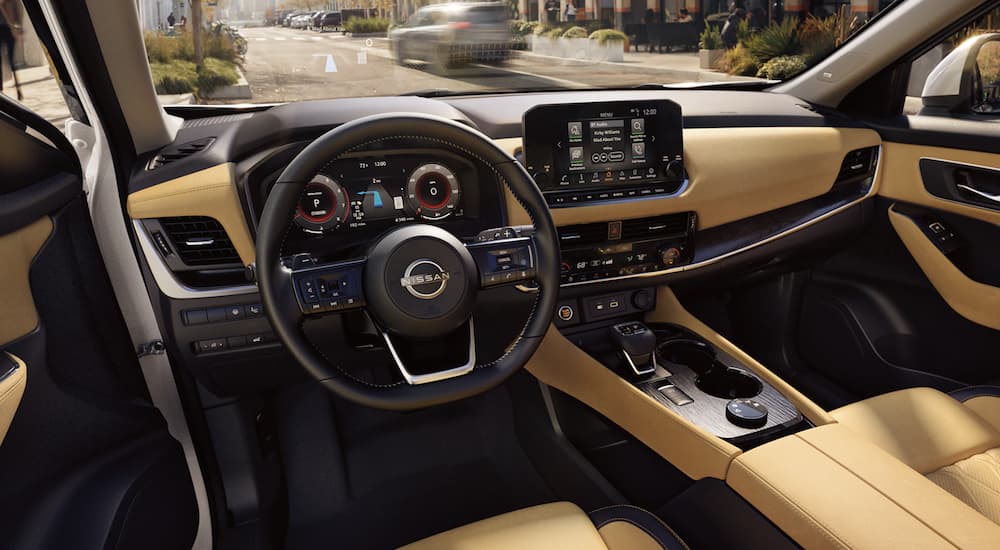 The tan and black interior of a 2023 Nissan Rogue shows the steering wheel and infotainment screen.