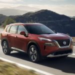 A red 2023 Nissan Rogue is shown from the side driving on an open road after leaving a Nissan Rogue dealer.