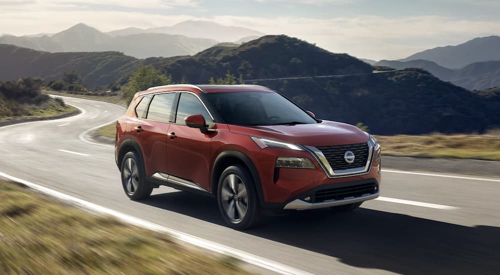 A red 2023 Nissan Rogue is shown from the side driving on an open road after leaving a Nissan Rogue dealer.