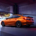 An orange 2022 Honda Civic Si is shown from the rear at an angle in an urban area.